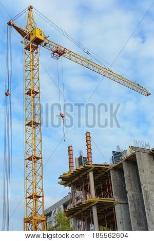 Yellow construction cranes and unfinished building with metal-concrete structure on a background of blue sky with white clouds. Vertical photo.