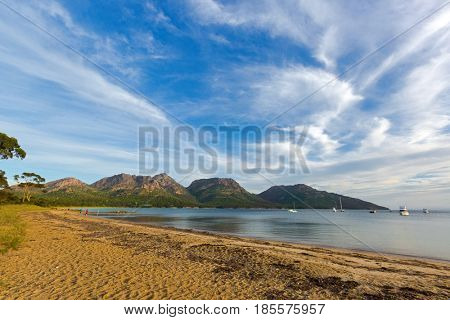 People walking on Freycinet national park beach in the evening, Hazards mountain range can be seen from Coles Bay in East coast of Tasmania, Australia