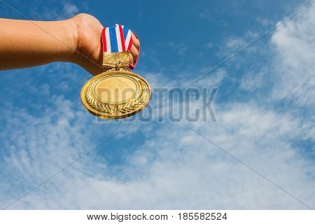 winner hand raised and holding gold medals against blue sky. success award concept