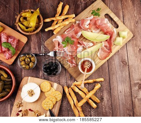 Italian antipasti wine snacks set. Cheese variety Mediterranean olives pickles Prosciutto di Parma with melon salami and wine in glasses over black grunge background