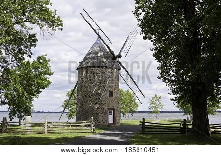 Notre Dame de Ile Perrot, Quebec - June 20 2014 --  Wide landscape of trees and foliage in front of a lake with a rock fire pit and three post wood hanger on the grass in the foreground in Notre Dame de Ile Perrot Quebec on a sunny day in June.