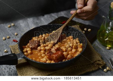 a frying pan with potaje de garbanzos, a spanish chickpeas stew with chorizo and serrano ham, on a rustic wooden table