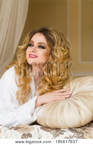 Beautiful seductive woman flirting with the camera lying on the bed with in White bathrobe looking up with a coquettish look.