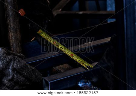 Closeup of a construction worker in hard hat using a measuring tape to mark cut line on a board. Focus is on the mans hands and tape measure.