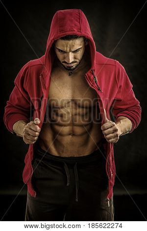 Muscular bodybuilder undressing, opening red hoodie sweater on naked muscle torso on light background