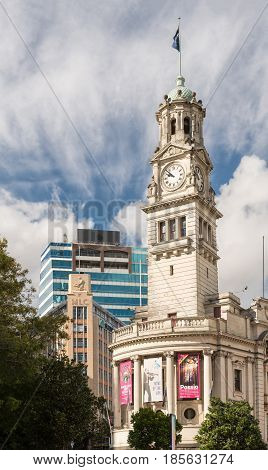 Auckland New Zealand - March 4 2017: The white stone Clock Tower of town hall with theater posters and flag. Green vegetation and blue sky with white clouds.