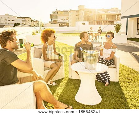 Attractive group of people socialising in an urban envronment on a green lawn on a warm summer afternoon, enjoying the sun on their skin during sunset.