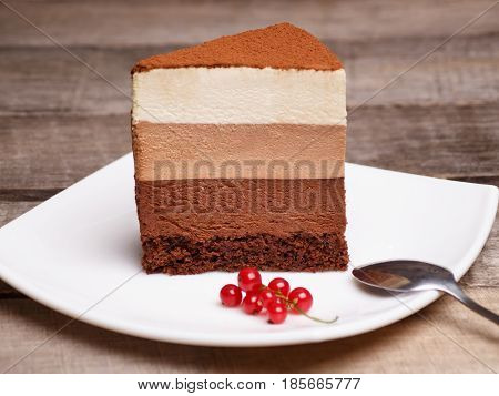slice of the three chocolate mousse cake on a white plate against a wooden background