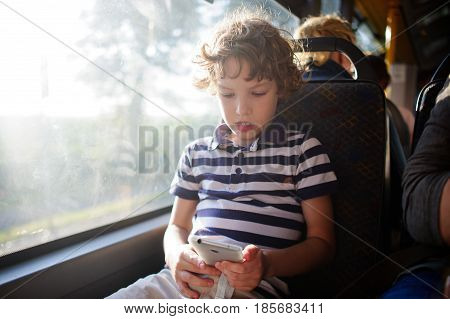 A small passenger of a city bus with a smartphone in hand. The boy sits at the window and looks with interest at the screen of the smartphone.