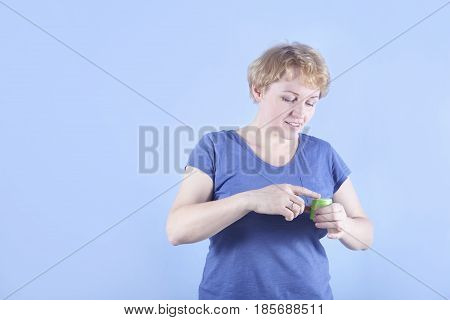 Pretty average age woman using anti-aging cream on blue background