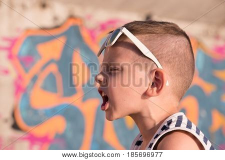 beautiful screaming boy in fashion sunglasses on background of graffiti wall
