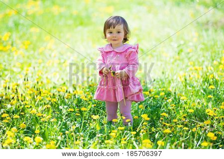 Girl in pink dress with dandelion on green grass