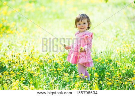 A little girl in a pink dress is laughing in a clearing with dandelions