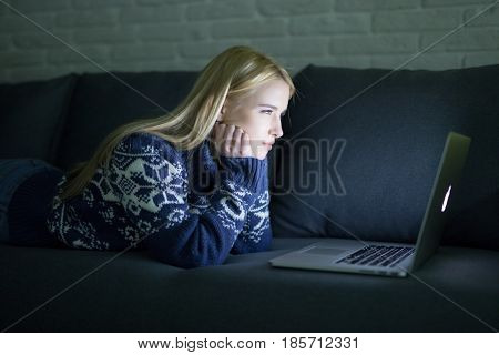 Happy Woman Lying On The Sofa With Her Laptop At Night At Home In The Sitting Room