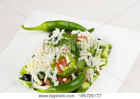 Traditional classic Shopska salad with tomatoes, peppers, cucumbers and cheese in white dish on white wooden table. Bulgarian cuisine, Balkan culture