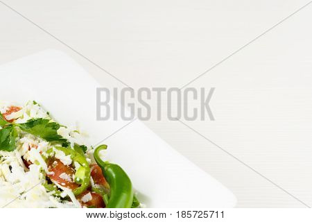 Traditional classic Shopska salad with tomatoes, peppers, cucumbers and cheese in white dish on white wooden table. Bulgarian cuisine, Balkan culture