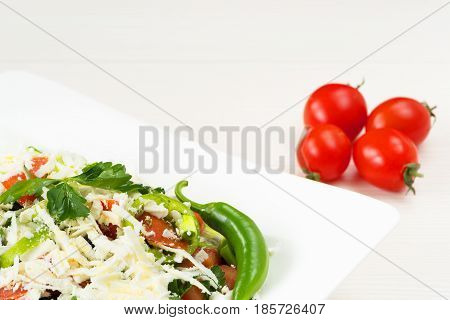 Traditional classic Shopska salad with tomatoes, peppers, cucumbers and cheese in white dish on white wooden table. Bulgarian cuisine, Balkan culture