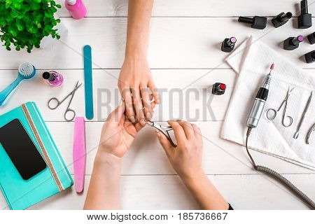 Manicure for the client. Close-up of the hands of a manicurist and client on a wooden background. Nail care. Manicure set and nail polish.