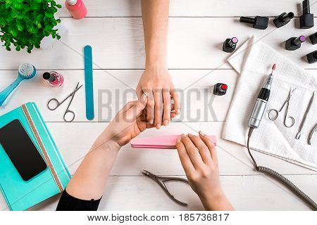 Manicure for the client. Close-up of the hands of a manicurist and client on a wooden background. Nail care. Manicure set and nail polish.
