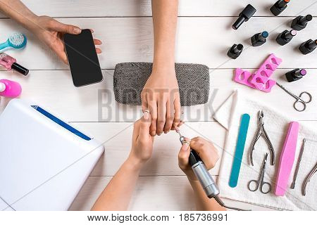 Manicure for the client. Close-up of the hands of a manicurist and client on a wooden background. Nail care. Manicure set and nail polish.
