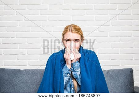 Blonde Woman Sneezing In A Tissue On Sofa In The Living Room
