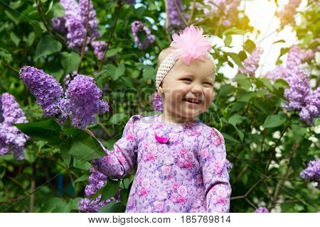 Beautiful little girl appy smiling and smells lilac flowers in spring park. Childhood. Cute kid's face over nature background. Cheerful child's portrait, soft focus.