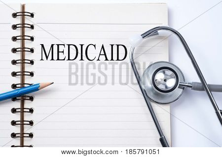 Stethoscope on notebook and pencil with MEDICAID words as medical concept