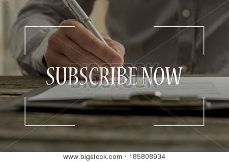 Subscribe now text over conceptual business scene with male hand signing contract or subscription form with a pen on a rustic wooden desk.