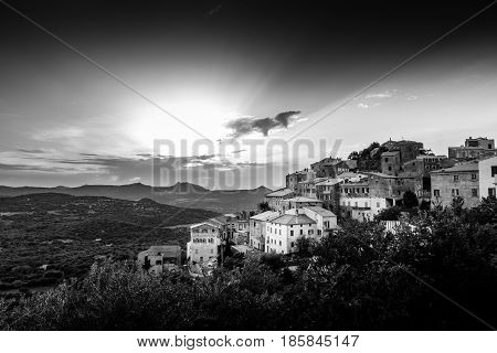 Black & White image of ancient hilltop village of Belgodere in the Balagne region of Corsica lit up by a dramatic evening sunset