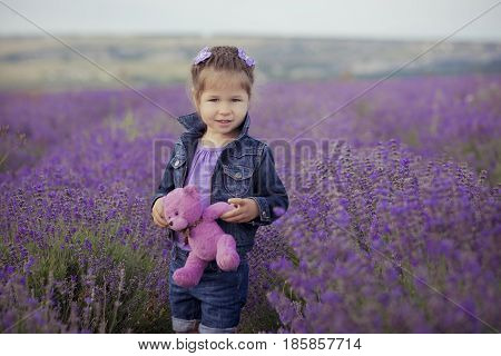 Pretty young girl sitting in lavender field in nice hat boater with purple flower on it