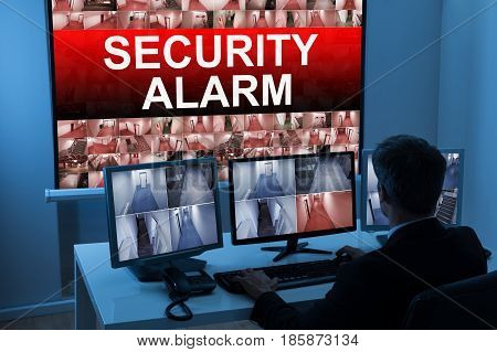 Male Operator Monitoring Multiple CCTV Footage With Security Alarm Text On Screen