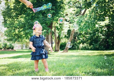 Portrait of cute adorable little Caucasian girl child in blue dress standing in field meadow park outside making soap bubbles lifestyle childhood