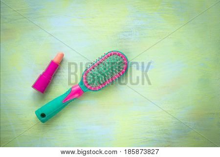 Green and pink hairbrush lipstick on a light wooden background