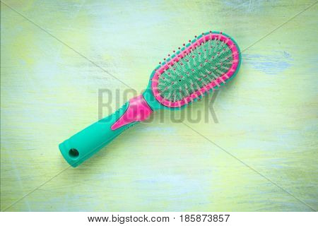 Green and pink hairbrush on a light wooden background