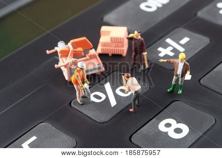 constatly changing interest rates / fixing the problem concept closeup of miniature figurine of workers reparing percentage button on a big black calculator
