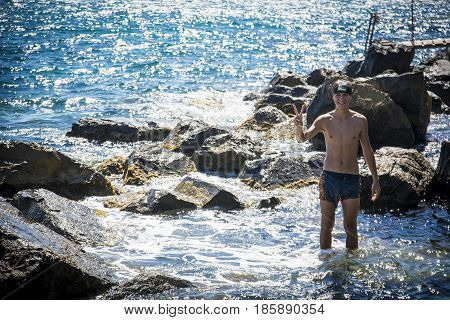 Teenger in swimming suit standing in sea water by rocks, looking at camera