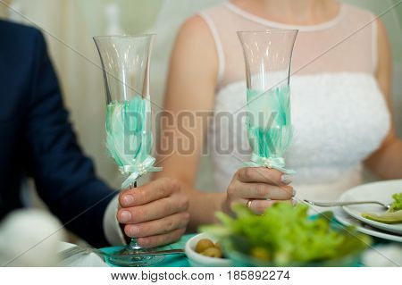 Bride And Groom Hold Champagne Flutes Decorated With Mint Feathers