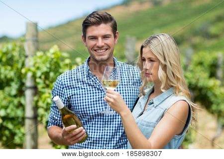 Young couple holding wine bottle and glass at vineyard
