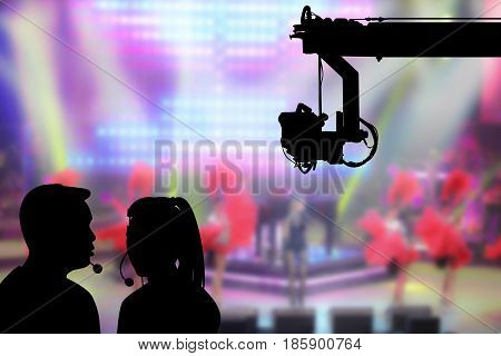 Silhouette image of the female director and cameraman or photographer talking or consulting to working with hanging cemara on crane on blurry concert on stage background in television studio