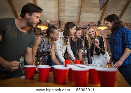 Happy friends playing beer pong game on table in bar