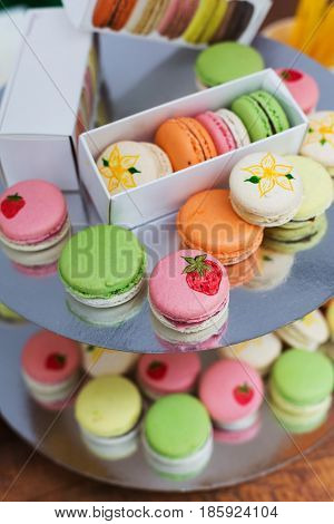 Beautiful Macarons choice. Plenty of colorful french cookies, meringue based confectionery desserts on serving plate at counter bar for sale. Pastel colors, packed in boxes and stacks, vertical image