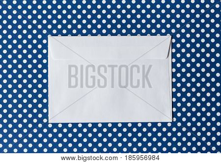 White paper envelope on a blue background polka dot in the center of the frame. Top View.