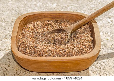 Old wheat species - grain-like triangular buckwheat seeds - in a rustic wooden shell with a wooden spoon. 