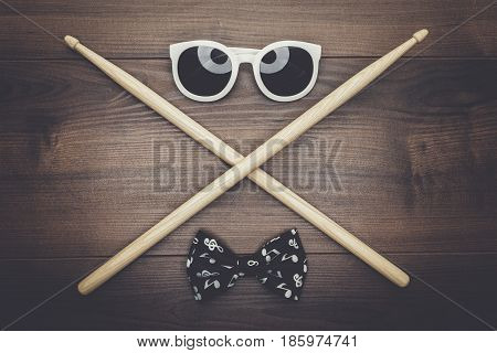 pair of wooden drumsticks crossed on wooden table, sunglasses and bow tie