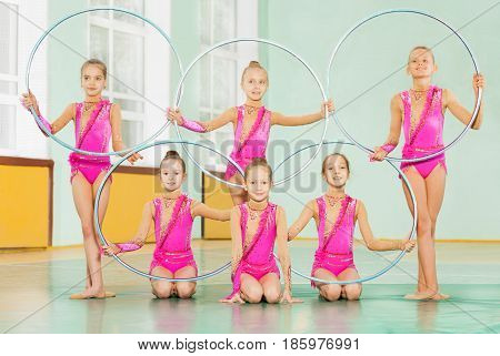 Group of six gymnast girls posing with rings in the gym