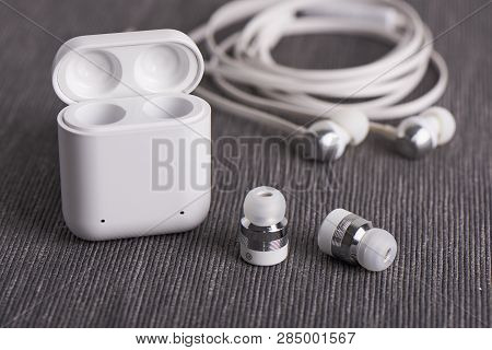 Wireless Cordless Bluetooth Earbuds With Chargeable Case On A Background Of Cable Earphone