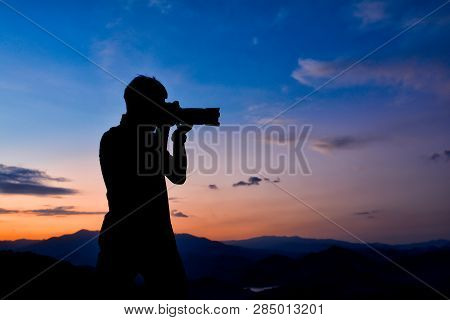 Silhouette Of A Man Who Is Professional Photographer Is Using A Dslr Camera At Twilight,orange And B