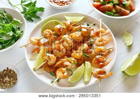 Prawns, Shrimp Skewers With Greens, Spices, Lime And Sauce On White Plate Over Wooden Table. Grilled