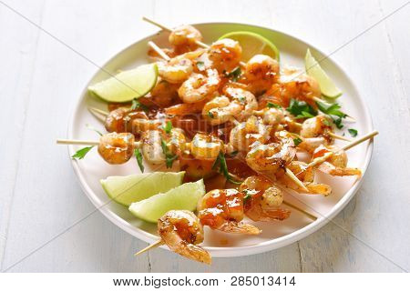 Prawns Skewers With Greens, Spices, Lime And Sauce On White Plate Over Wooden Table. Grilled Shrimp 