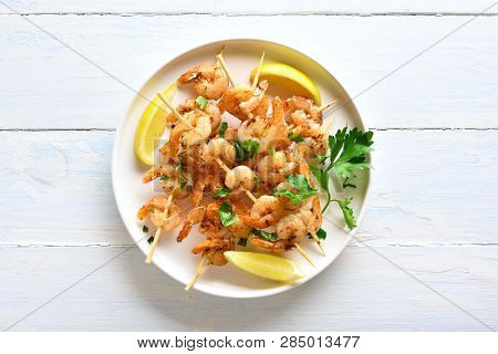 Grilled Shrimp Skewers. Prawns Skewers With Greens, Spices And Lemon On White Plate Over Wooden Tabl